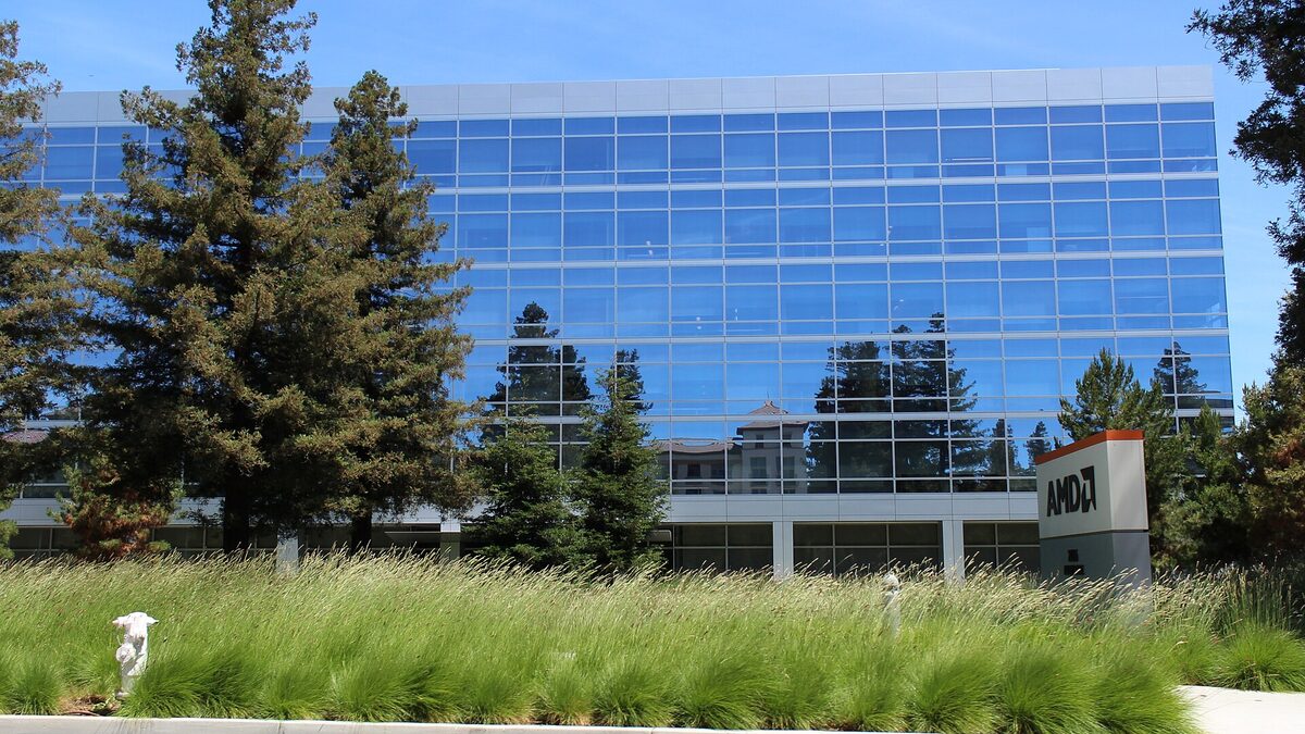 AMD's glass-fronted Santa Clara headquarters behind ornamental grasses, with the AMD sign on a low monument by the sidewalk