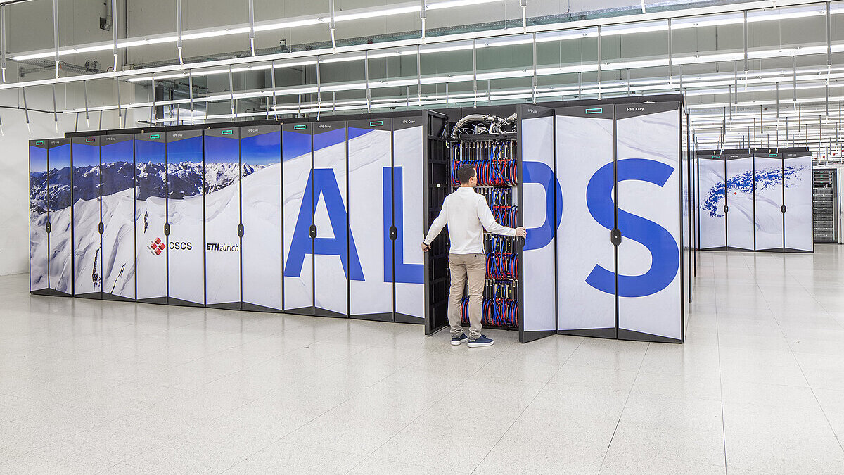 Rows of supercomputer cabinets in a data hall, a technician working at an open rack
