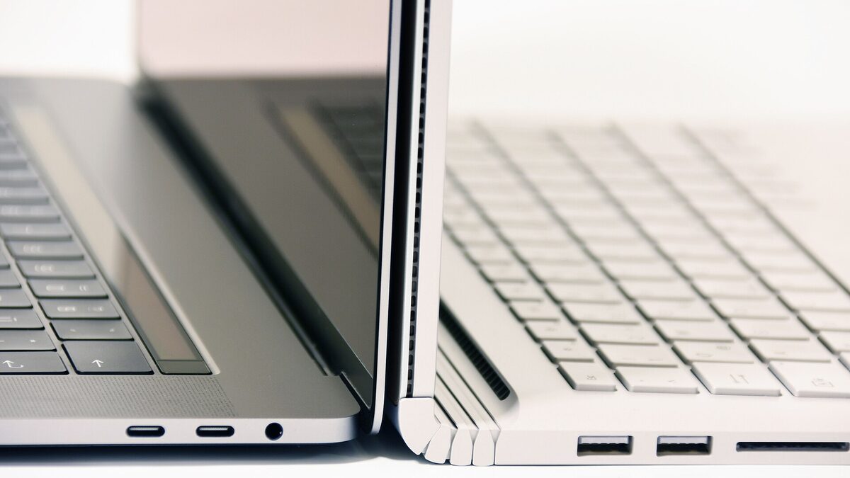 A MacBook Pro beside a Surface Book, both open on a white surface, USB-C ports in view