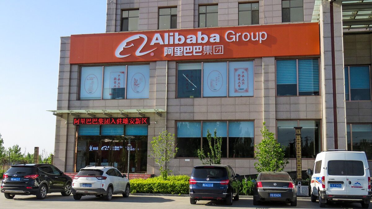 An Alibaba Group office building with the company's orange logo sign above the entrance and cars parked outside.